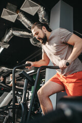 Fototapeta na wymiar An active man with beard training in gym, riding a stationary exercise bike. Sport and quarantine.