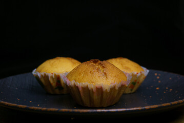 Three cupcakes on a plate on a black background