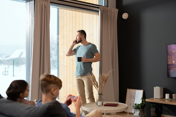 Young relaxed businessman having drink and talking on mobile phone by window