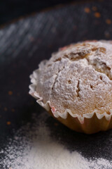 cupcake in powdered sugar on a plate on a black background