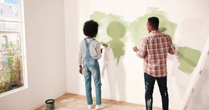 Young african american couple painting wall in new apartment. Handsome man in plaid shirt tells his wife how to apply paint.
