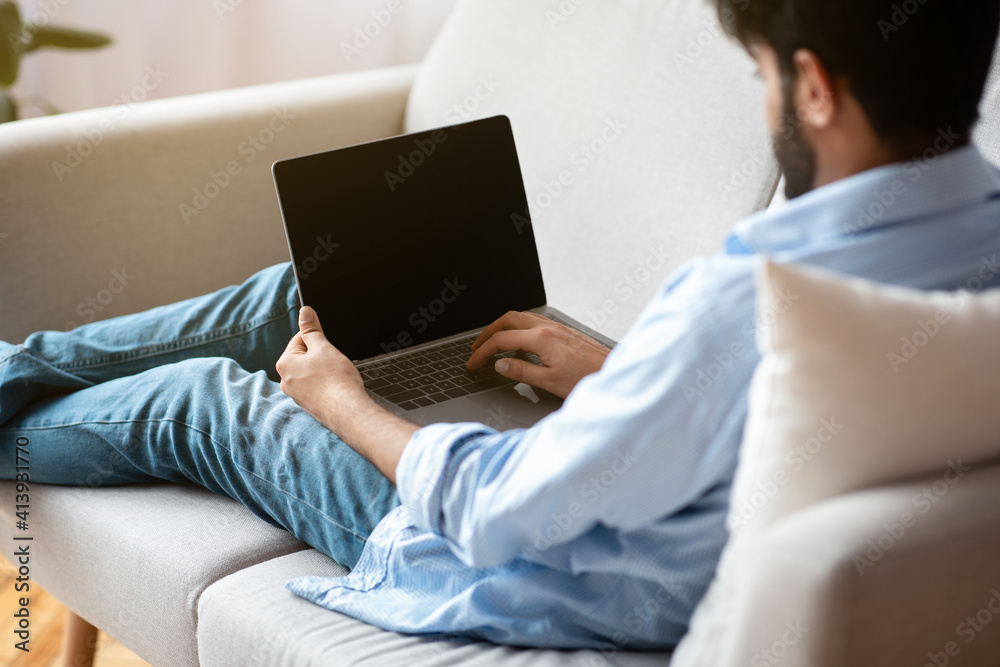 Poster unrecognizable eastern man using laptop computer with blank black screen at home