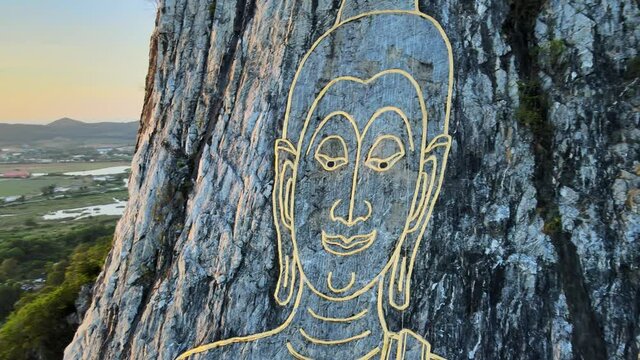 4k Close up Aerial view: image of Buddha, sitting cross-legged, engraved with gold into the northern face of a limestone hill in Khao Chi Chan, Thailand. Cinematic footage of Buddha Mountain at dawn