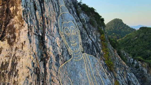 4k Aerial view: image of Buddha, sitting cross-legged, engraved with gold into the northern face of a limestone hill in Khao Chi Chan, Thailand. Close up Cinematic footage of Buddha Mountain at dawn