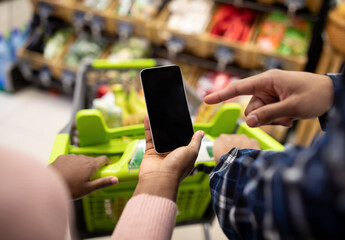 Unrecognizable black couple holding smartphone with empty screen at supermarket, mockup for your mobile app or website