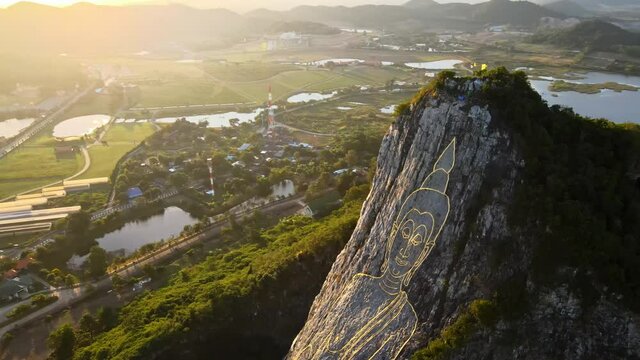 4k Top down Aerial footage of carved Buddha Image made from Gold on a cliff at Khao Chee Chan, Pattaya, Thailand. Golden light with sun glares on the image of Buddha Engraved with gold on the mountain