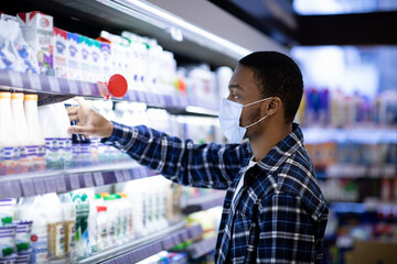 Side view of African American man in face mask choosing dairy products at supermarket during...