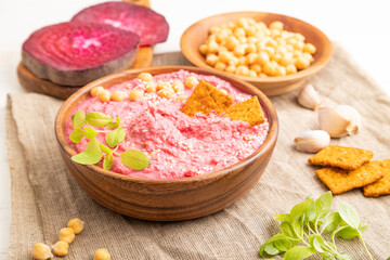 Hummus with beet and microgreen basil sprouts in wooden bowl on a white wooden background. Side view, close up.