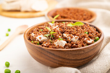 Quinoa porridge with green pea and chicken in wooden bowl on a white wooden background. Side view, selective focus.