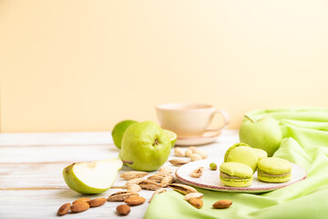 Green macarons or macaroons cakes with cup of coffee on a white and orange background. Side view, selective focus, copy space.
