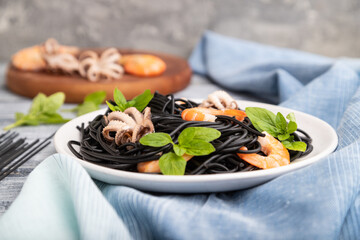 Black cuttlefish ink pasta with shrimps or prawns and small octopuses on gray wooden background. Side view, selective focus.