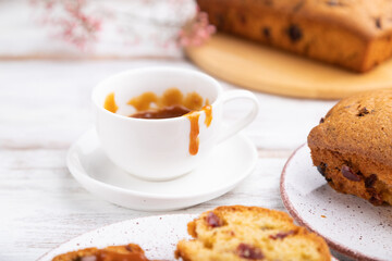 Homemade cake with raisins, almonds, soft caramel and a cup of coffee on a white wooden background. Side view, selective focus.