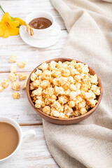 Popcorn with caramel in wooden bowl and a cup of coffee on a white wooden background. Side view.