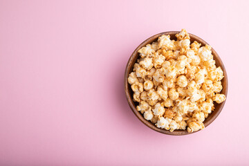 Popcorn with caramel in wooden bowl on a pastel pink background. Top view, copy space.