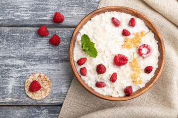 Rice flakes porridge with milk and strawberry in wooden bowl on gray wooden background. Top view, close up.