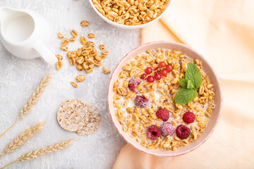Wheat flakes porridge with milk, raspberry and currant in ceramic bowl on gray concrete background. Top view, close up.