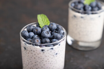Yogurt with blueberry and chia in glass on black concrete background. Side view.