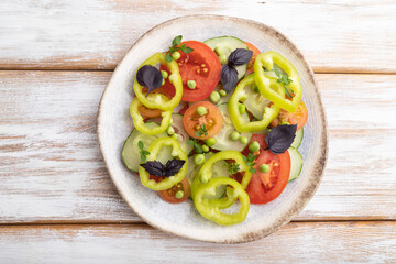 Vegetarian salad from green pea, tomatoes, pepper and basil on white wooden background. top view.