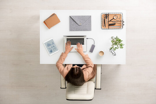 Overview of young businesswoman in formalwear sitting by desk in front of laptop