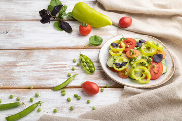 Vegetarian salad from green pea, tomatoes, pepper and basil on white wooden background. Side view, copy space.