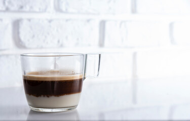 Glass Cup of tricolour Cappuccino, with chocolate croissant, and piece of chocolate. Wooden wall background and white floor.