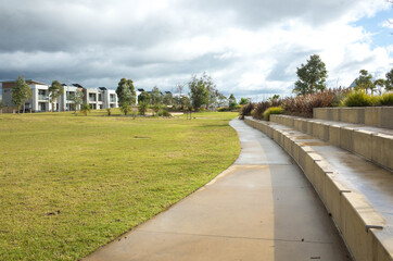 A concrete pedestrian footpath in a park with some modern residential houses or  homes in the distance. A public suburban park in an Australian neighbourhood.