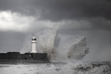Wintry and stormy seas crashing over breakwater with lighthouse