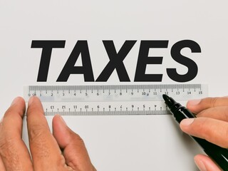 Business and tax concept. Phrase TAXES written on white background with plastic ruler and hands holding marker pen.