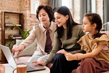 Three generation family of females in casualwear sitting in front of laptop