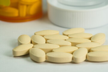 A collection of small oval-shaped white pills with orange pill container in background blurred
