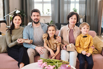 Happy family of five sitting in row on large comfortable couch in living room