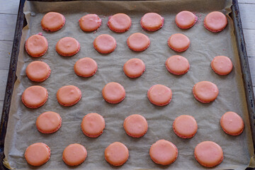 Pink homemade macaron cookies halves with feet on parchment paper on a baking sheet