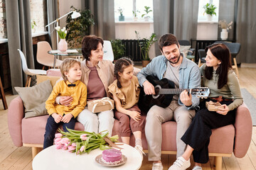 Happy family of five talking and listening to singing of young man with guitar