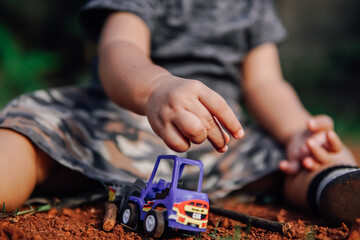 the boy's hand was playing with his toy on the dirty ground