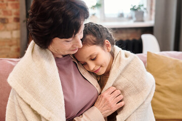 Affectionate cute little girl embracing her grandmother while resting on couch