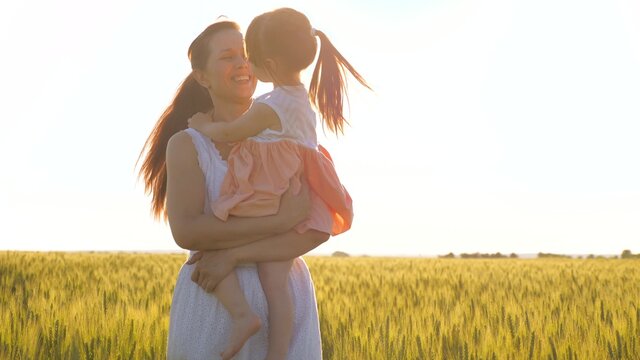 Mom and little daughter play on the ripe wheat field, hug and kiss. A mother walks with child in a wheat field. Happy family travels. The baby is in mom's arms. Farmer woman and child in field