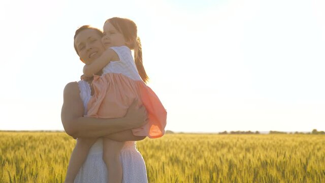 Mom and little daughter play on the ripe wheat field, hug and kiss. A mother walks with child in a wheat field. Happy family travels. The baby is in mom's arms. Farmer woman and child in field