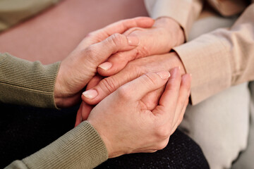 Hands of young supportive female counsellor holding those of mature woman