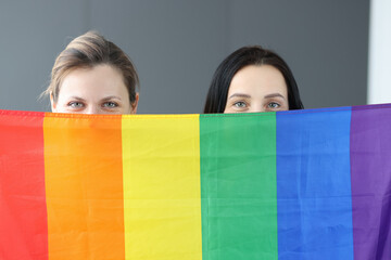 Two women hold lgbt flag in front of them