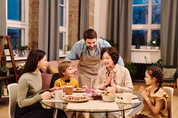 Young man in apron bending over served table among his family during dinner
