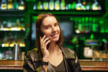 Happy young brunette woman in smart casualwear talking on smartphone in bar