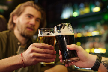 Hands of two friendly guys clinking with glasses of beer in front of camera