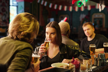 Young brunette female drinking beer and looking at her boyfriend during chat