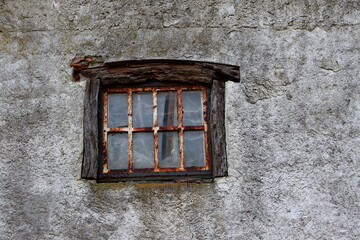 An old small window with a wooden frame and a rusty lattice in a gray wall.