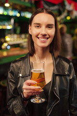 Young smiling brunette woman in casualwear having glass of beer in pub