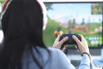 Female gamer sits with her back holding game joystick and plays game on the computer © megaflopp