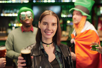 Young cheerful brunette woman with glass of beer toasting against guys in hats