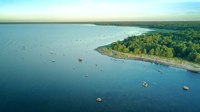 Aerial forward motion over beautiful coastline landscape, green coast, calm water surface and scattered rocks, drone motion blue sky horizon