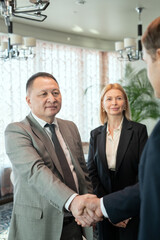 Successful mature businessman in suit greeting foreign partner by handshake