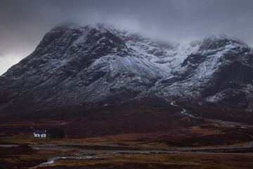 low mountain cabin in Glencoe, Scotland, Uk. typical highland building with snowy mountain Stob Dearg in the background. Snowy atmosphere in winter, after a big storm